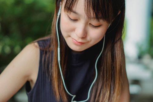 Free Crop calm young Asian female in blue tank top listening to music with light blue earphones and looking down Stock Photo