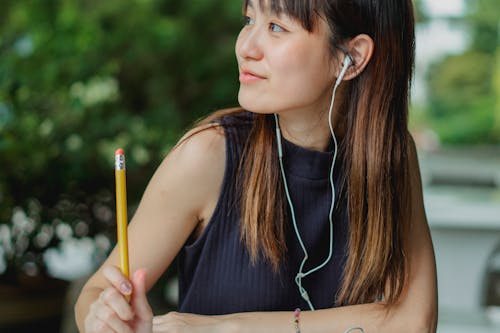 Free Happy young Asian student listening to music while studying at table in park Stock Photo