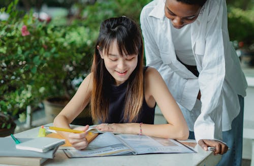 Positive multiracial female students working on home task in park