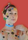Young female with tailoring meter on neck and spools of threads on head touching shoulder while looking at camera