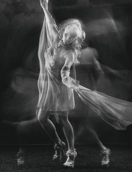 Black and white photo of a ballerina in flowing dress on dark background.