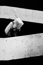 Grayscale Photo of Man in White Long Sleeve Shirt and Pants Sitting on Concrete Wall
