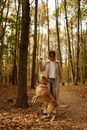 Woman in White Long Sleeve Shirt Standing Beside Brown Dog