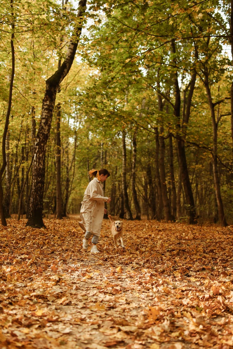 A Woman And Dog Running In The Forest