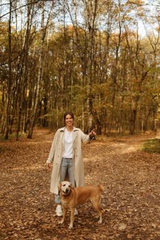 秋天的森林里，绿树成荫，一位微笑的女人和她的拉布拉多猎犬漫步其中