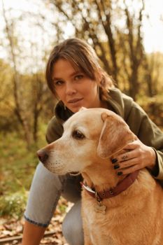 一名穿着绿色毛衣的女子和一只拉布拉多猎犬正在户外享受秋日时光
