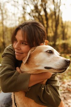 秋日阳光明媚的森林里，一位女士微笑着拥抱她的拉布拉多猎犬