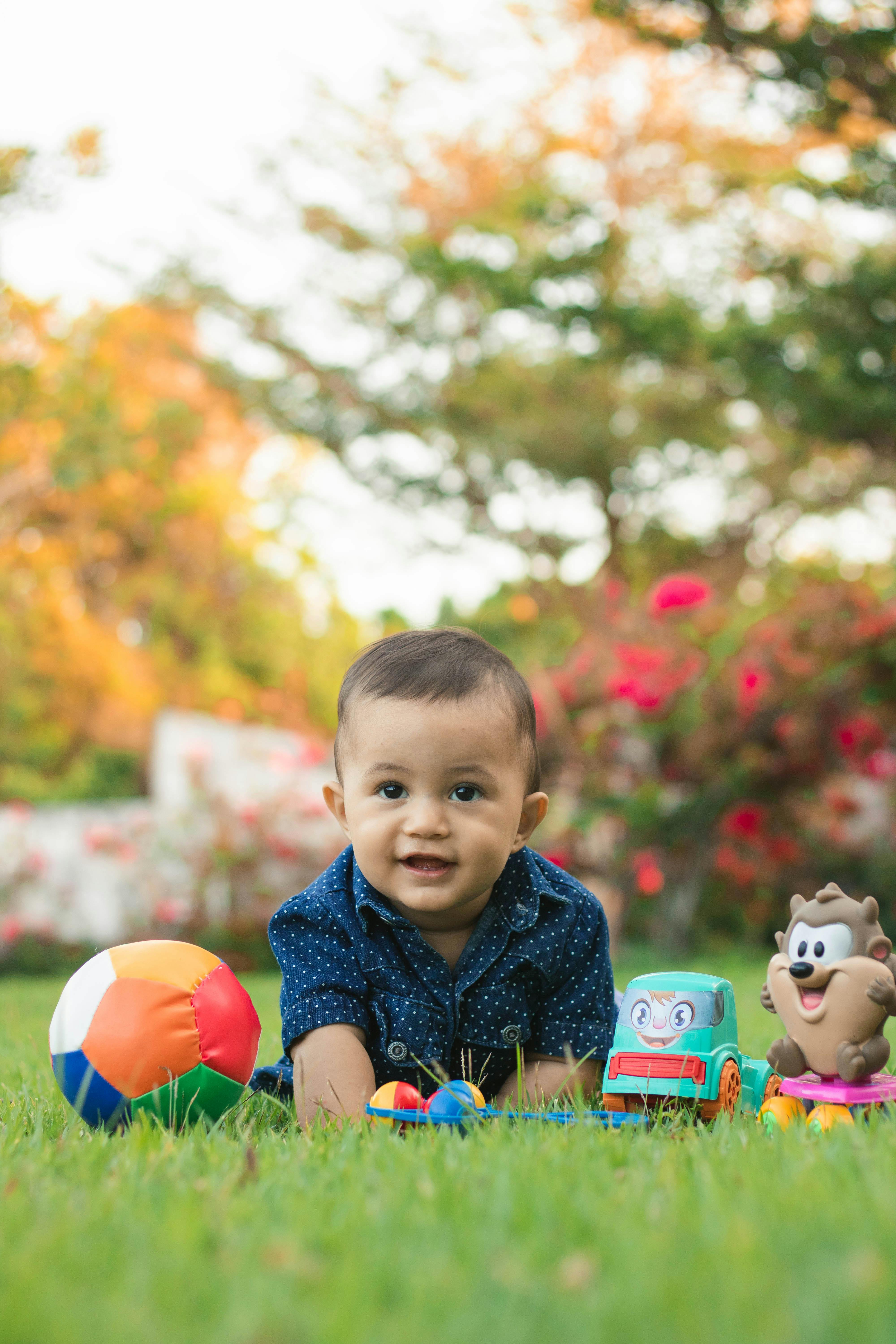 happy little boy sitting on grass amidst toys