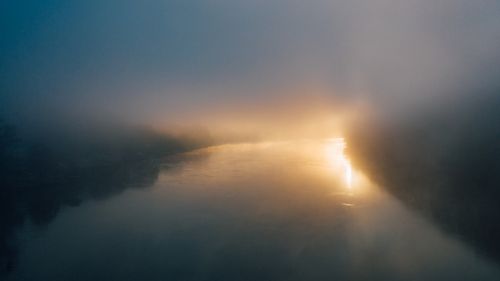 Free Scenic view of rippled river with glowing light between tree silhouettes under sky in mist at dusk Stock Photo
