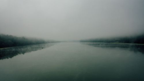 Free Scenic view of lake reflecting dark tree silhouettes under white sky in mist in twilight Stock Photo