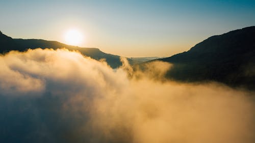 Scenic view of mount silhouettes near thick cloud under glowing sky with sun in evening