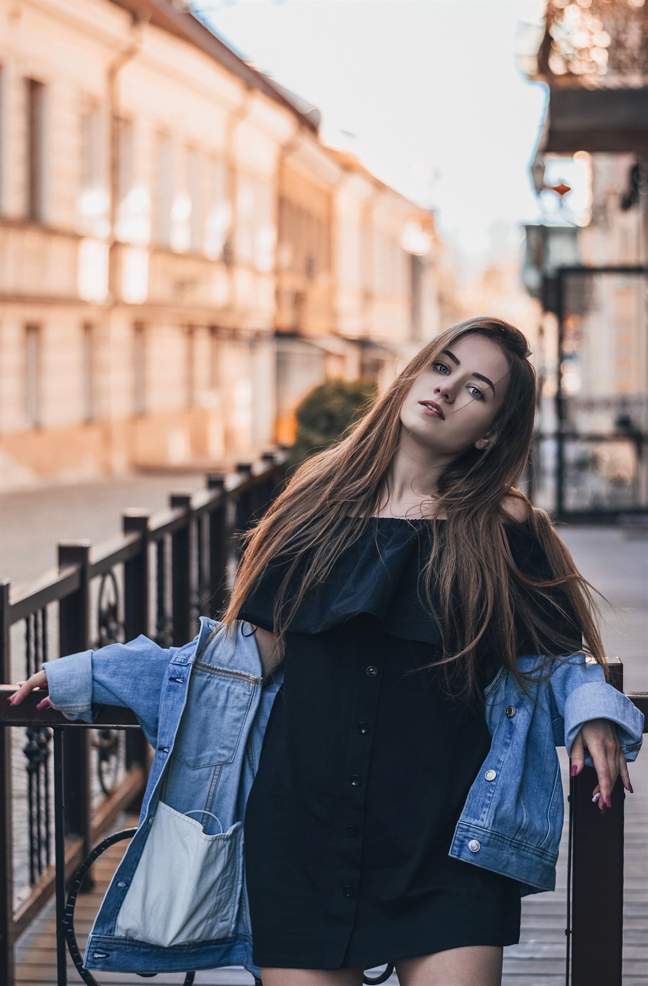 Woman in a black off-the-shoulder dress with a denim jacket draped over her shoulders.