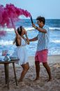 Full body side view of expressive couple with smoke bombs on sandy beach during gender party
