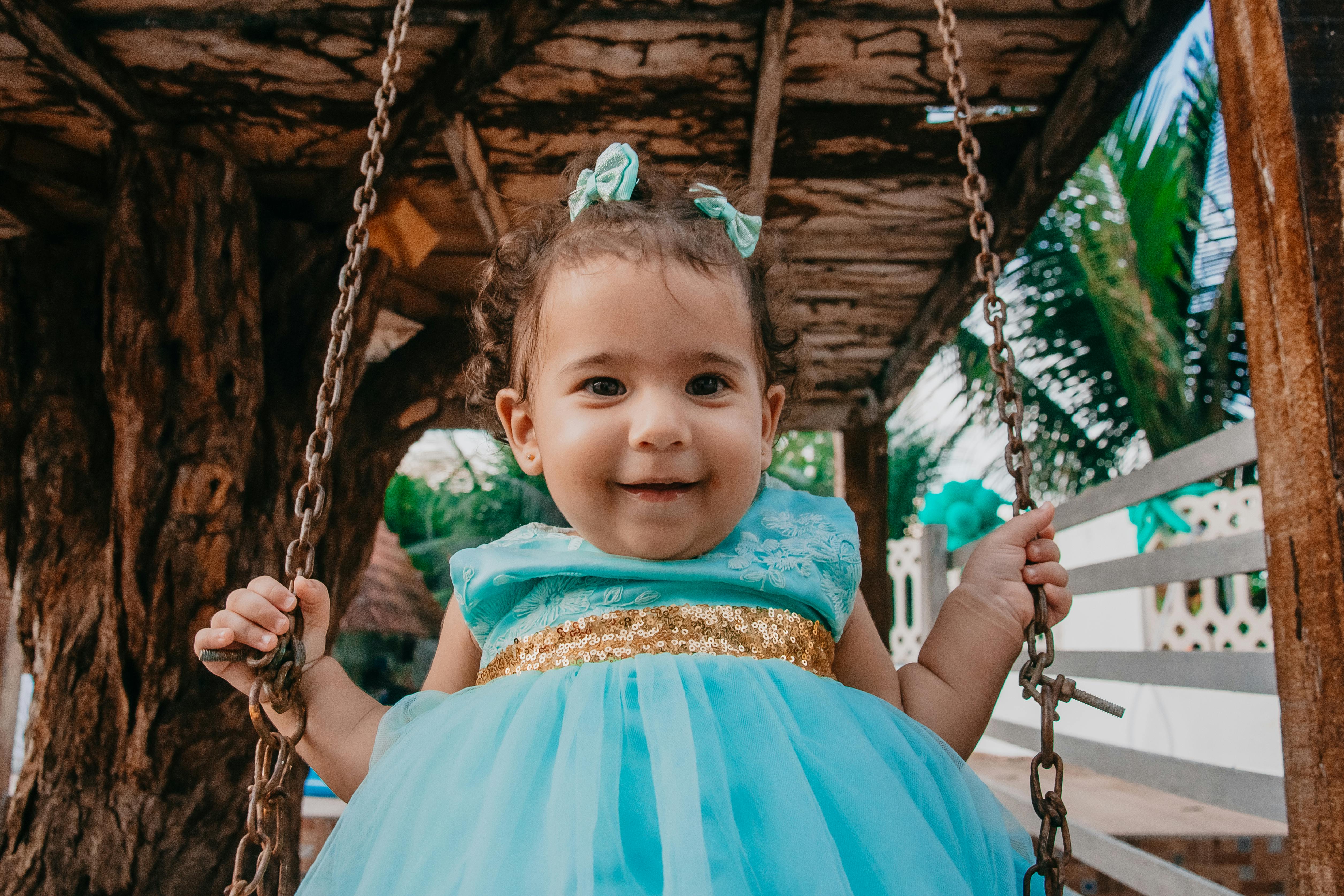 cute happy ethnic baby in stylish dress swinging on street