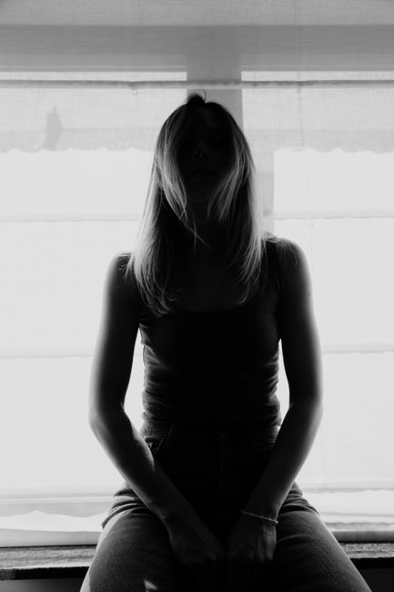 Black and white of faceless slim female resting on windowsill against bright light