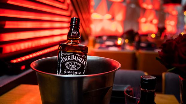 Close-up of a Jack Daniel's whiskey bottle in a bucket with red bokeh background.