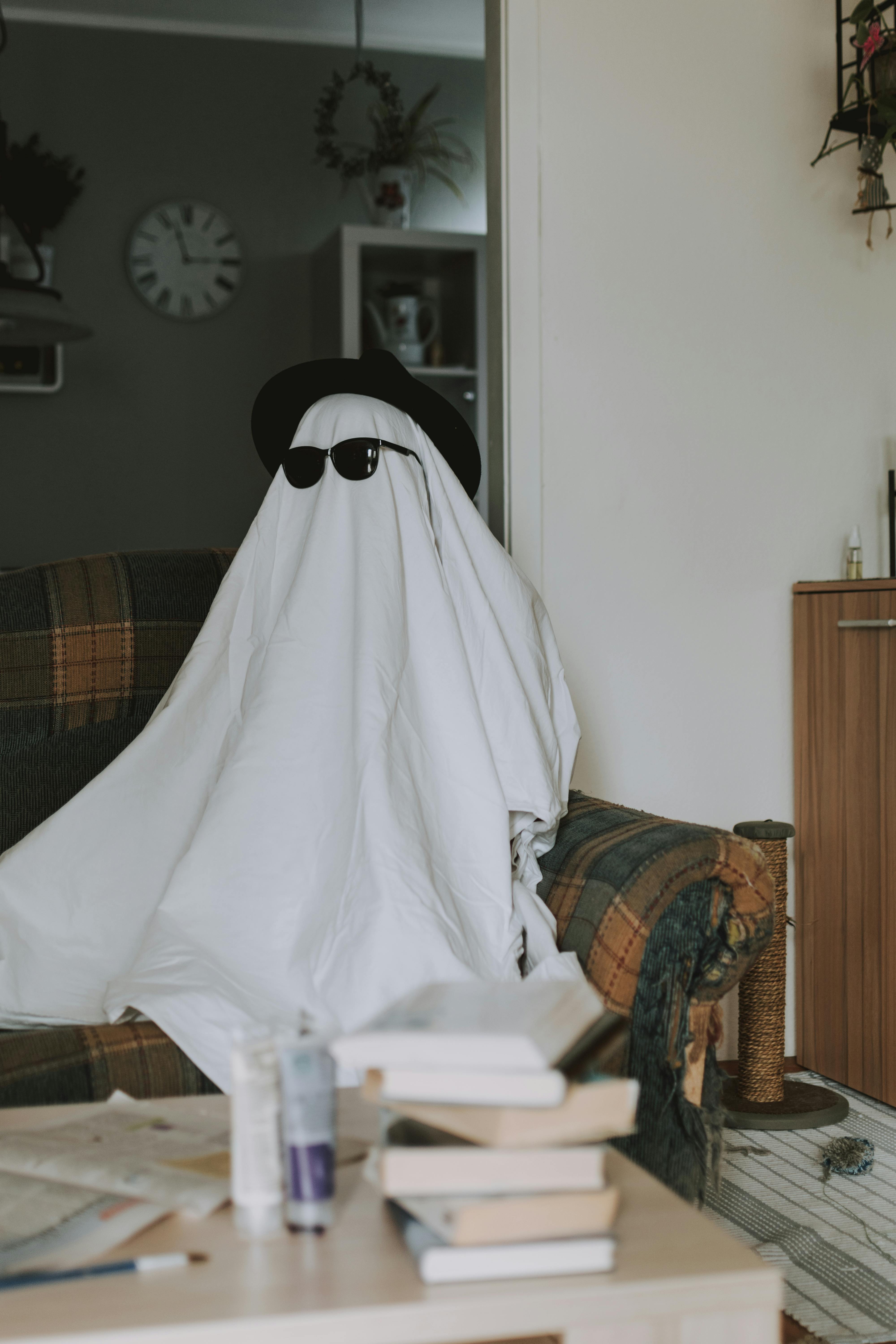 A funny ghost costume with sunglasses sitting on a living room sofa. Perfect for Halloween themes.