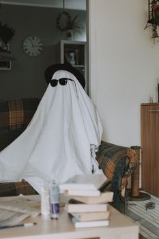 A funny ghost costume with sunglasses sitting on a living room sofa. Perfect for Halloween themes. — photo by lil artsy