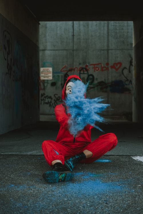 Free Full body of person in unusual outfit and scary mask sitting on ground and throwing blue powder Stock Photo