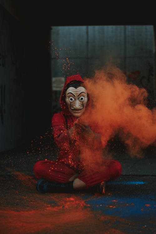 Full body of artistic creative person in costume and Dali mask spreading orange powder on street