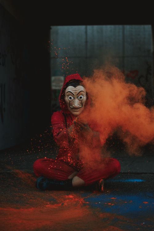 Free Full body of artistic creative person in costume and Dali mask spreading orange powder on street Stock Photo