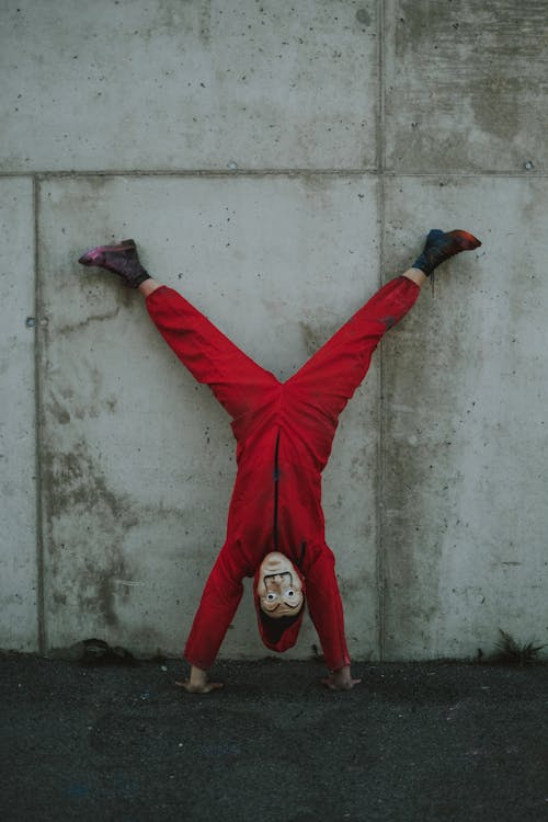 Full body of person in scary costume standing upside down leaning on concrete wall