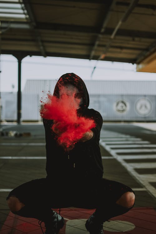 Man with face under mask in black outfit squatting while throwing powder around