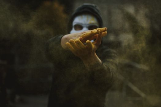 Selective focus of man hands covered with color powder wearing creepy mask and hoodie
