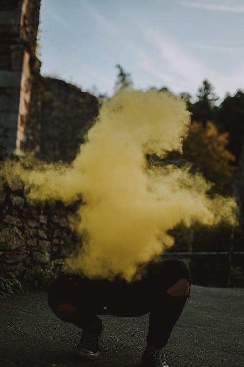 Anonymous male wearing black clothes squatting on street while throwing bright yellow powder