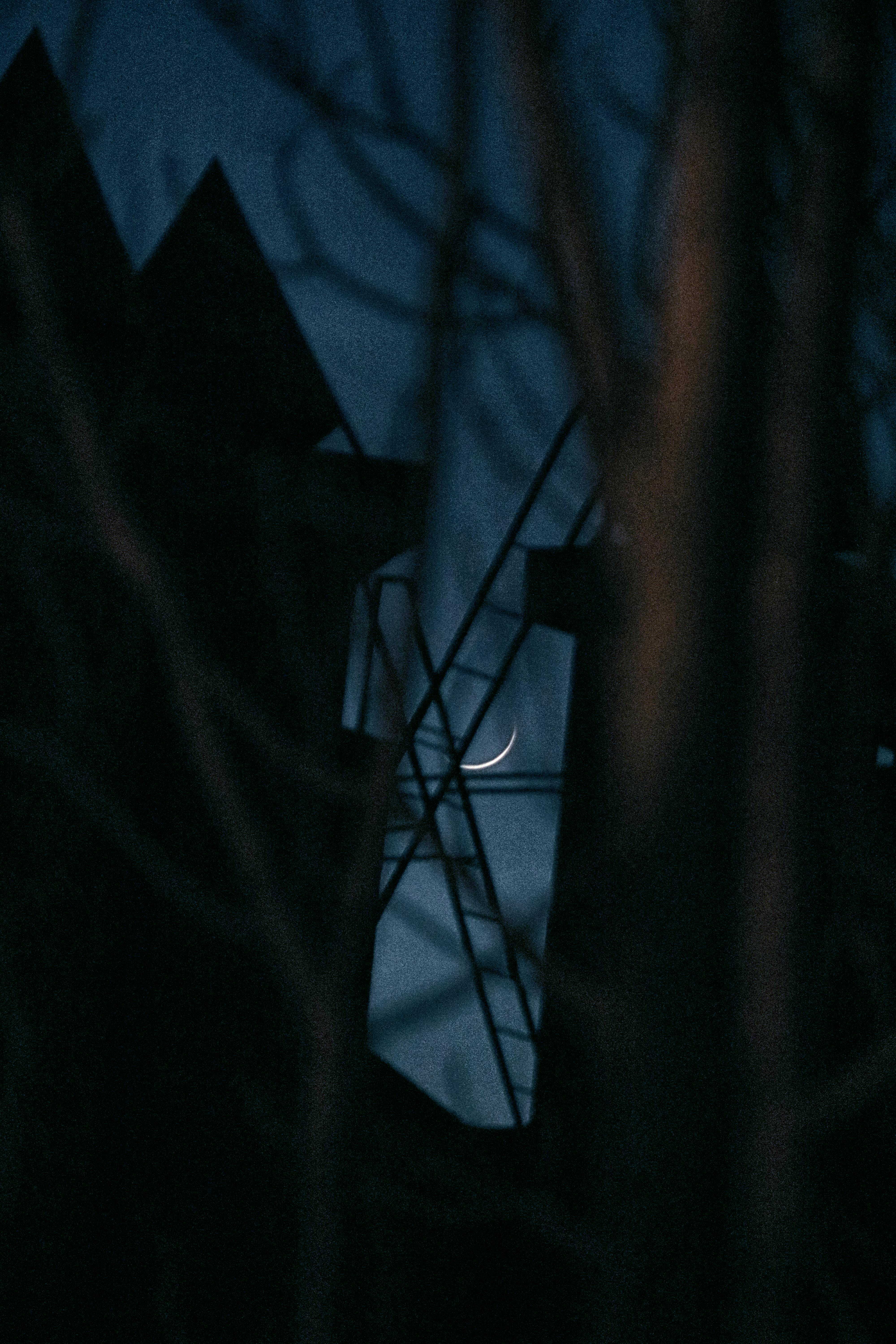 A crescent moon peeks through silhouetted structures at night, creating a mysterious ambiance.
