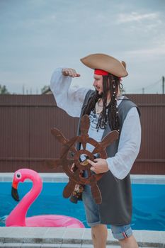 Side view of young actor in costume of pirate standing near outdoor swimming pool and looking away