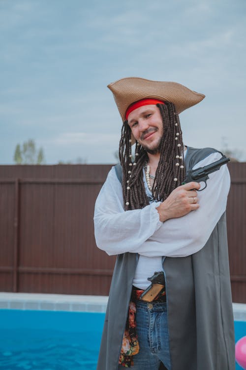 Joyful young male in pirate costume with toy gun standing near pool