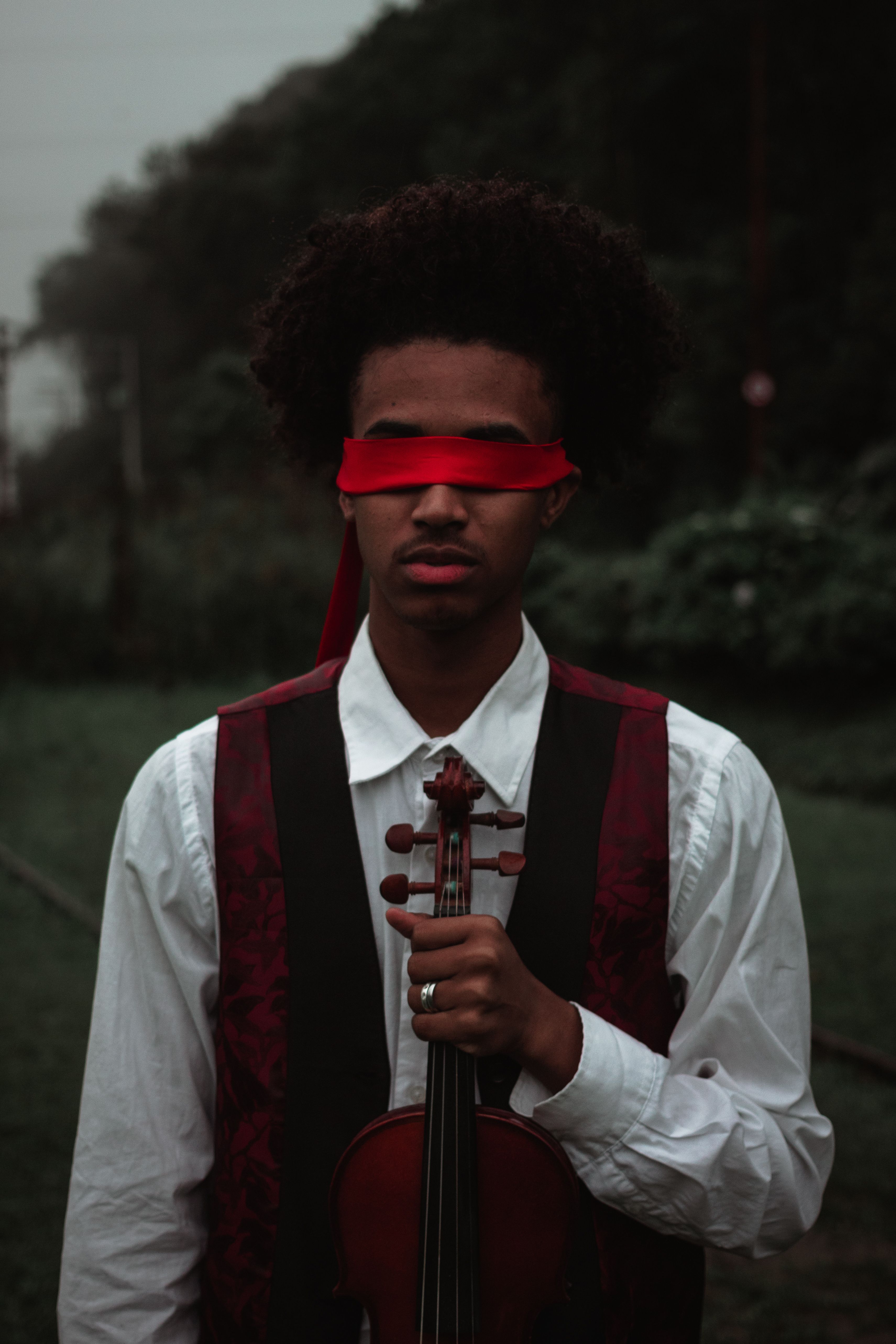 Concentrated blindfolded African American male in classic clothing holding violin for musical performance in nature