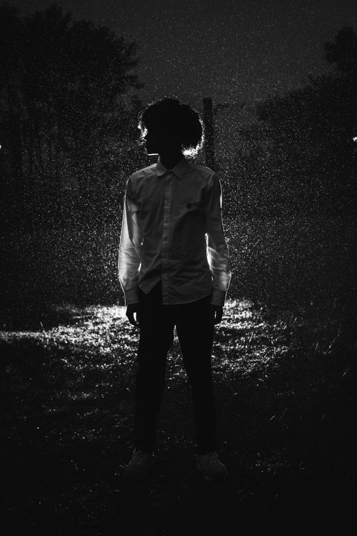Free Black and white full body of anonymous male in shirt and pants standing in darkness in back lit Stock Photo