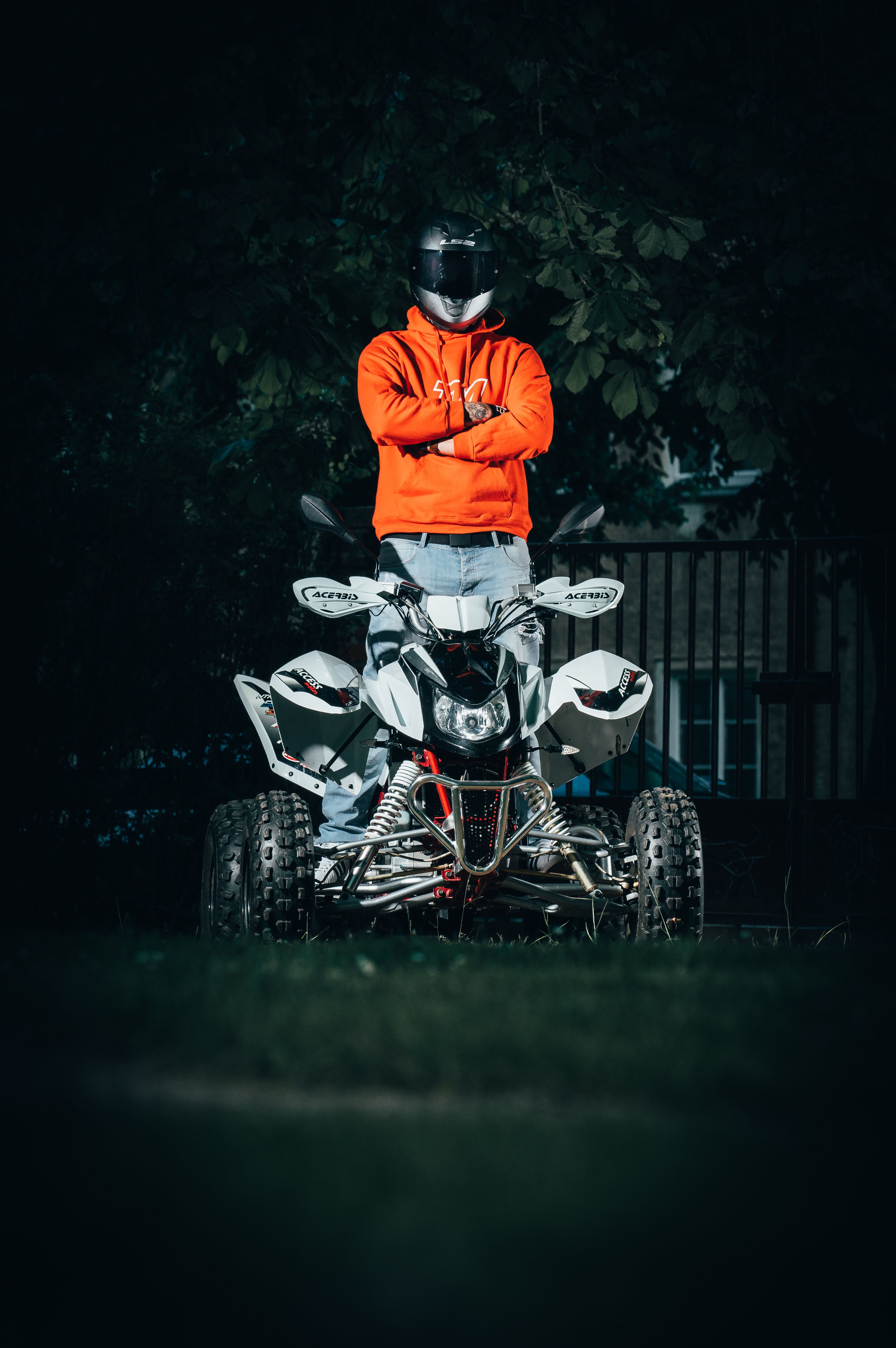 Man stands confidently on a quad bike wearing a helmet and bright hoodie outdoors.