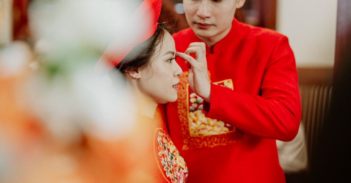 Crop ethnic man touching forehead of young beloved in traditional bridal red apparel during wedding ceremony