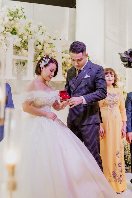 Ethnic man in elegant suit putting ring on finger of beloved woman in bridal dress during wedding ceremony
