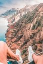 Person in White Sneakers Sitting on Brown Rock Formation Near Body of Water