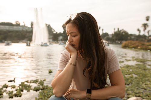 Free A thoughtful woman sits by a fountain, reflecting near a lake. Stock Photo