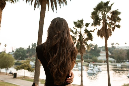 一名长发女子站在湖边，背影周围是风景优美的棕榈树