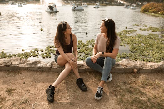 Two women sitting by a serene lake, enjoying a warm conversation on a sunny day.