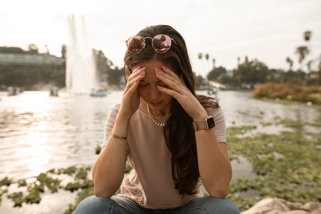 Free Distressed woman sitting on lakeside and touching face in despair Stock Photo