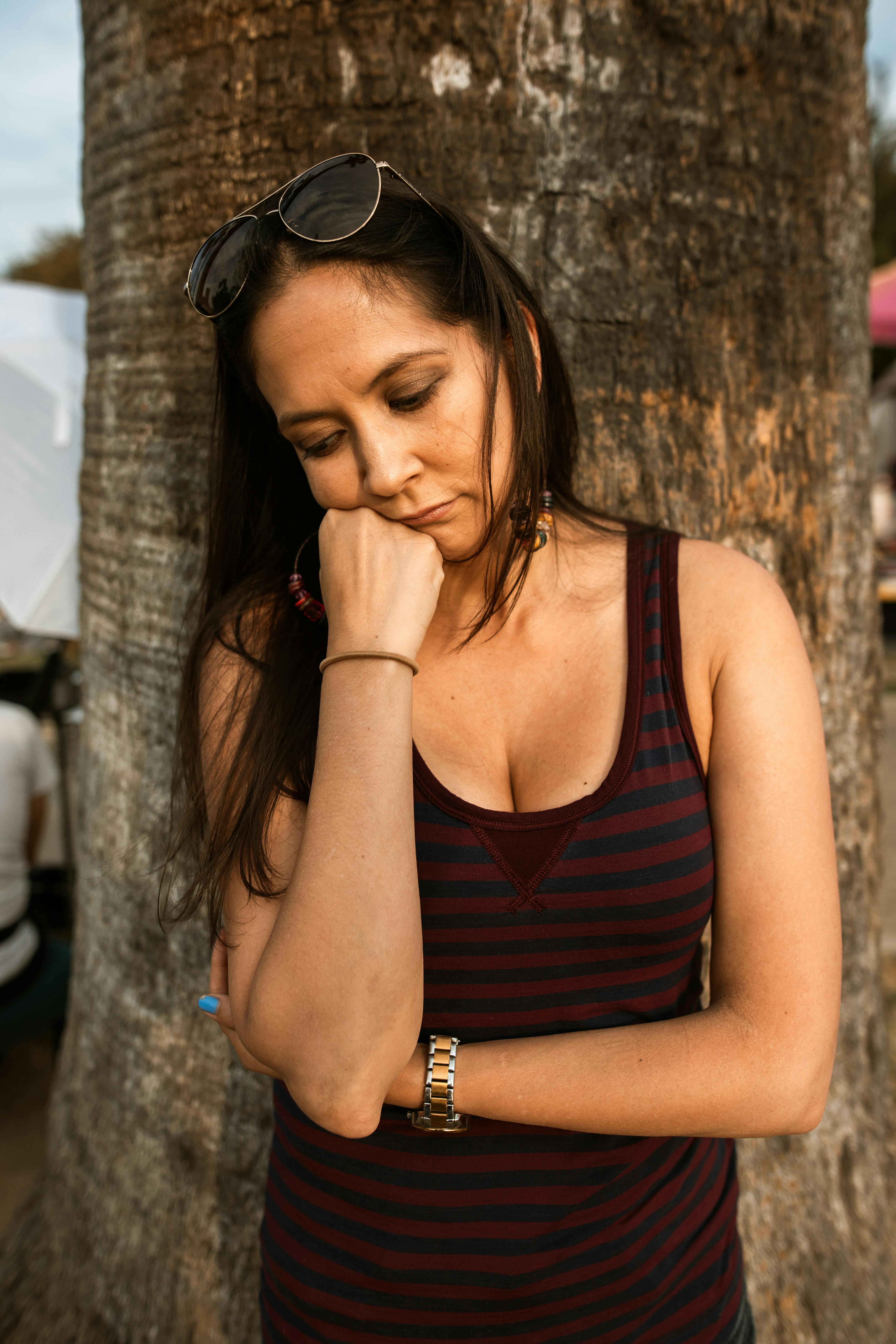 woman with hand on chin leaning on a tree trunk