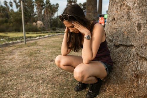 Mujer En Camiseta Negra Sin Mangas Y Pantalones Cortos Negros Sentada En Brown Rock