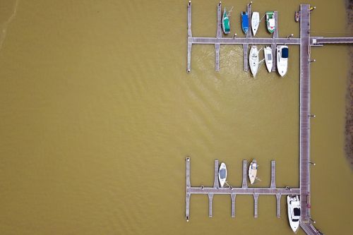 Free Drone view of brown sea surface and pier with sailboats and yachts in harbor Stock Photo