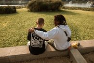 Man in White Long Sleeve Shirt and Black and White Backpack Sitting on Brown Concrete Bench