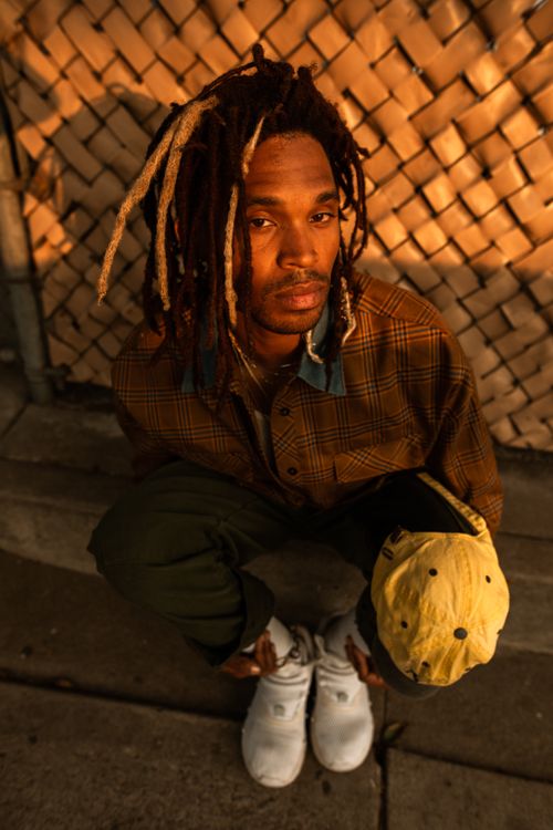 Free Urban portrait of a man with dreadlocks against a chain-link fence in warm light. Stock Photo