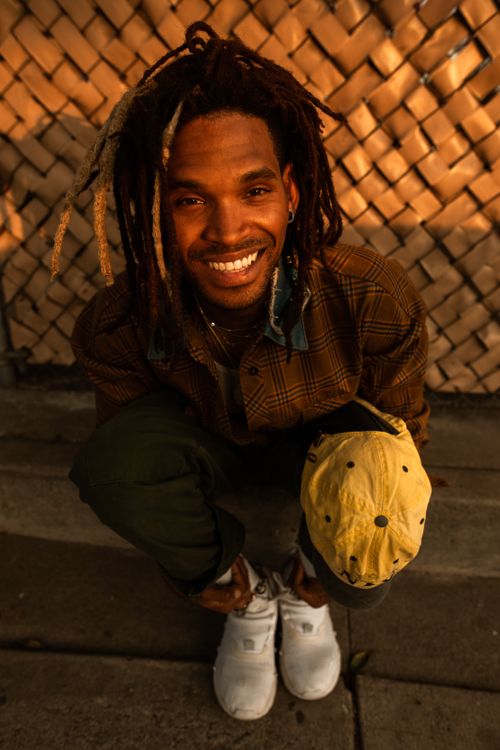 Free Happy man with dreadlocks smiling outdoors, wearing casual outfit under warm daylight. Stock Photo