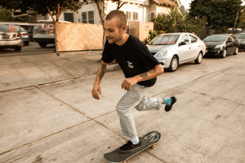 Man in Black Crew Neck T-shirt and Gray Pants Riding a Black Skateboard