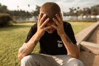 一名纹身男子捂着头坐在公园里，显得压力重重，陷入沉思